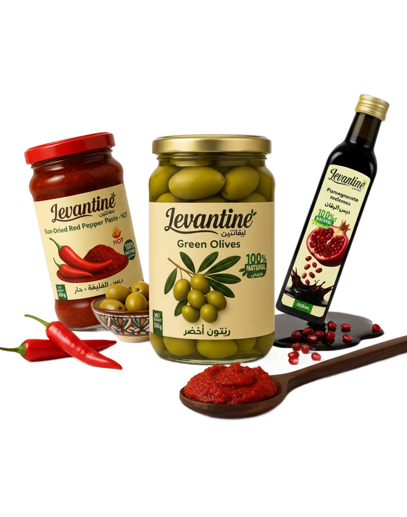 hero banner for levantinedeli.com on a white background. It features three Levantine brand products: a jar of Sun-Dried Red Pepper Paste, a jar of Green Olives, and a bottle of Pomegranate Molasses. The products are arranged dynamically with some ingredients like fresh red chilies, green olives in a small bowl, pomegranate seeds, and a spoonful of red pepper paste artfully placed around them. The text 'levantinedeli.com' and 'Taste the Authentic Levant' are at the top.